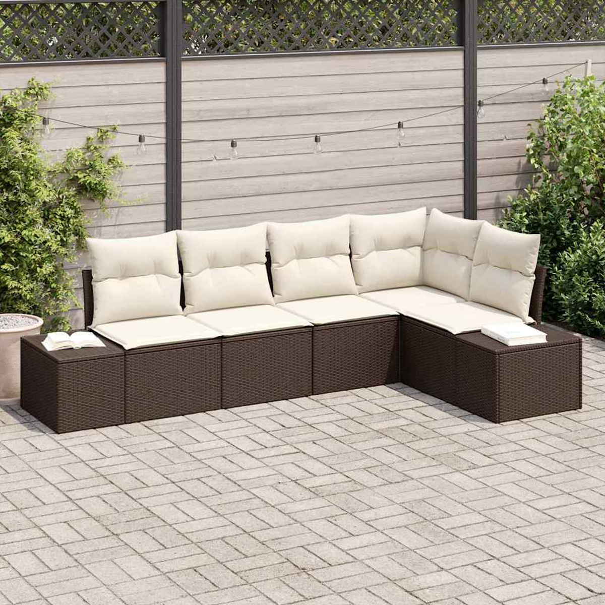 Ein L-förmiges braunes Outdoor-Sofa aus Korbgeflecht mit cremefarbenen Kissen steht auf einer Ziegelterrasse. Im Hintergrund sind ein Zaun und Grünpflanzen zu sehen.