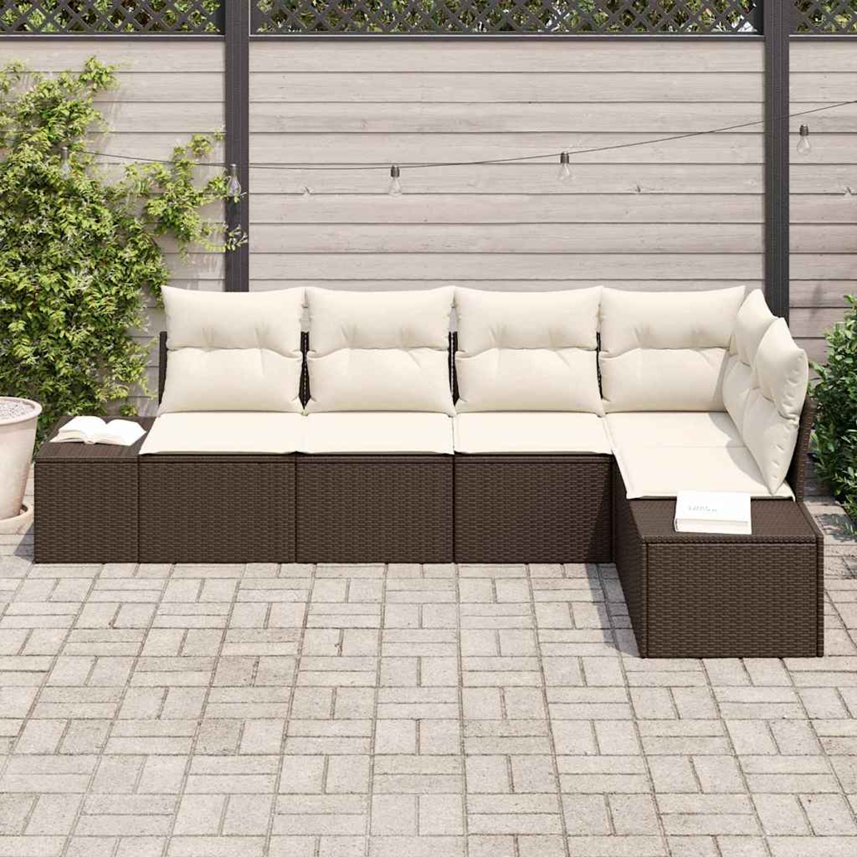 Ein Ecksofa im Freien mit cremefarbenen Kissen und brauner Korbbasis steht auf einer Steinterrasse. Ein Buch liegt auf der Seite.