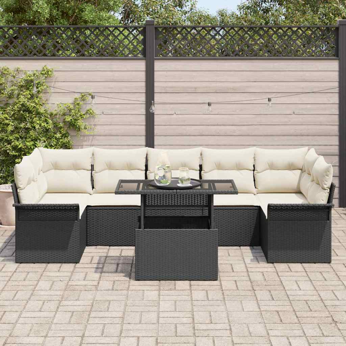 Schwarzes Outdoor-Korbsitzgruppen-Set mit cremefarbenen Kissen. Ein Glastisch und eine graue Backstein-Terrasse. Im Hintergrund ein Holzzaun.