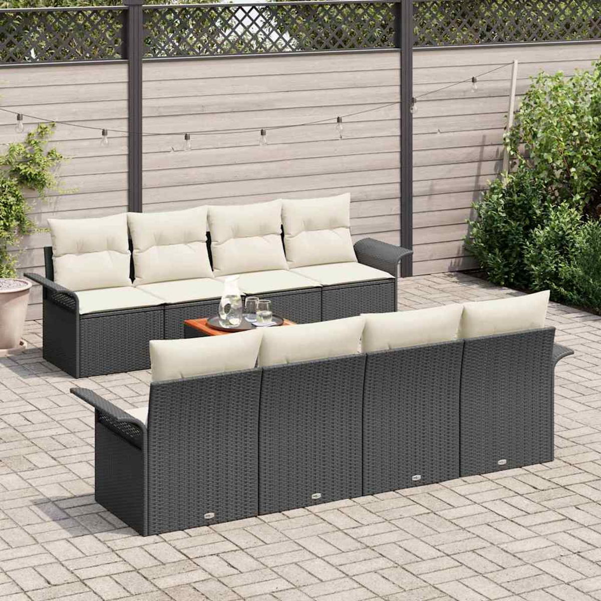 Zwei dunkelgraue Korbsessel mit cremefarbenen Kissen, ein kleiner Tisch mit Getränken, auf einer Terrasse mit Holzzaun und Grün im Hintergrund.