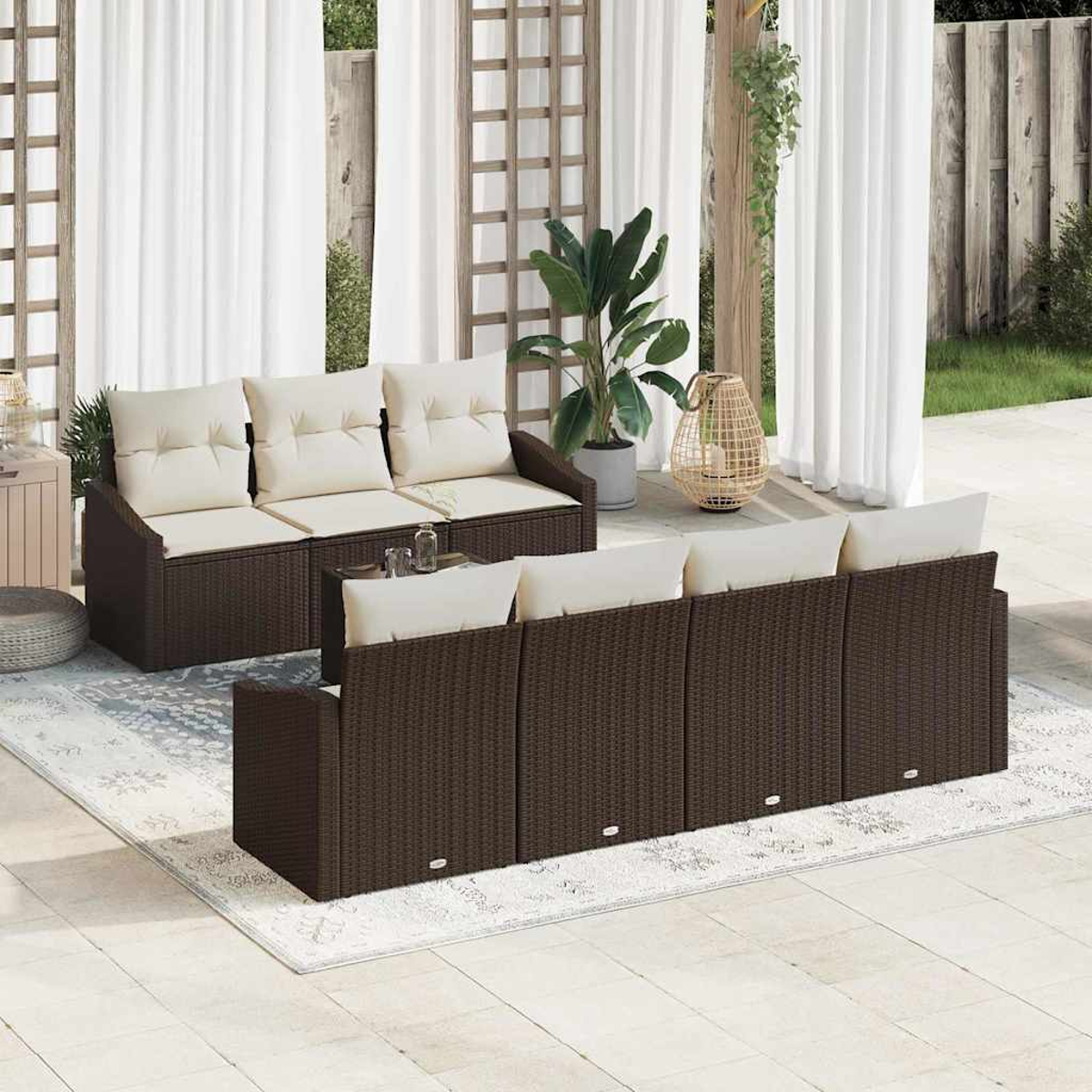 Gartenmöbel-Set. Braune Korbsessel mit cremefarbenen Kissen auf einem hellen Teppich. Weiße Vorhänge und Pflanzen im Hintergrund.