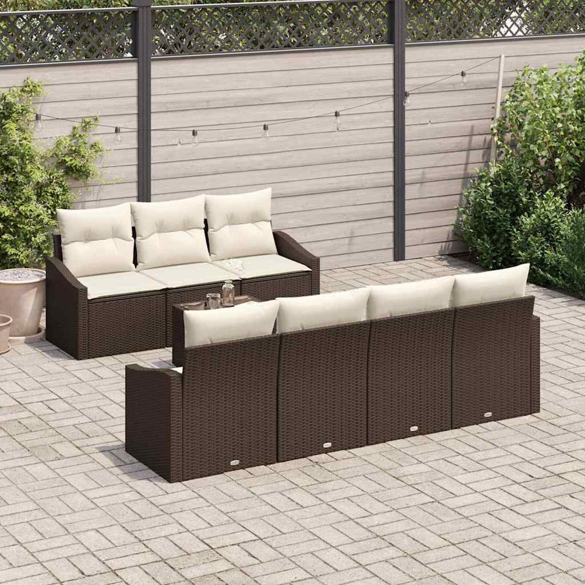 Zwei braune Korbsessel mit cremefarbenen Kissen auf einer Ziegelstein-Terrasse. Ein Holzzaun mit Lichterketten und Grünzeug im Hintergrund.