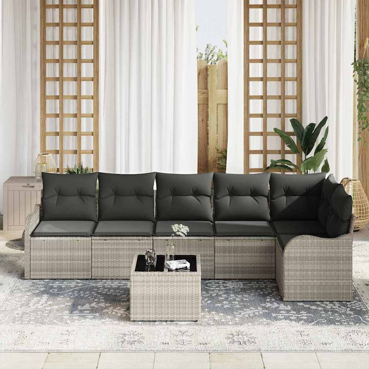 Outdoor-Ecksofa mit grauen Kissen, kleinem Tisch, Teppich und weißen Vorhängen. Im Hintergrund ist ein Holzgitter zu sehen.