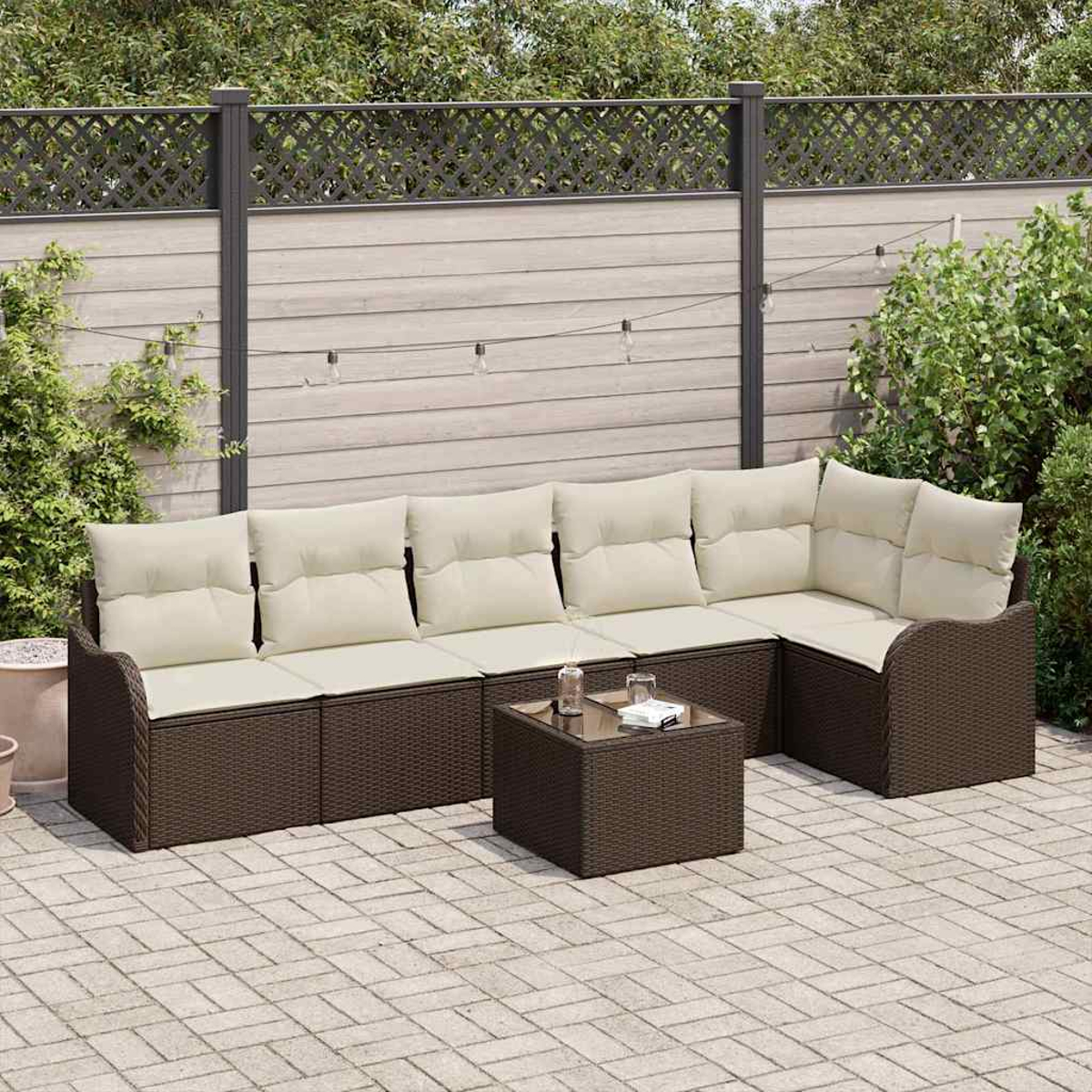 Ecksofa im Freien mit cremefarbenen Kissen und einem kleinen Tisch auf einer Backsteinterrasse. Im Hintergrund sind ein Zaun und Grün zu sehen.