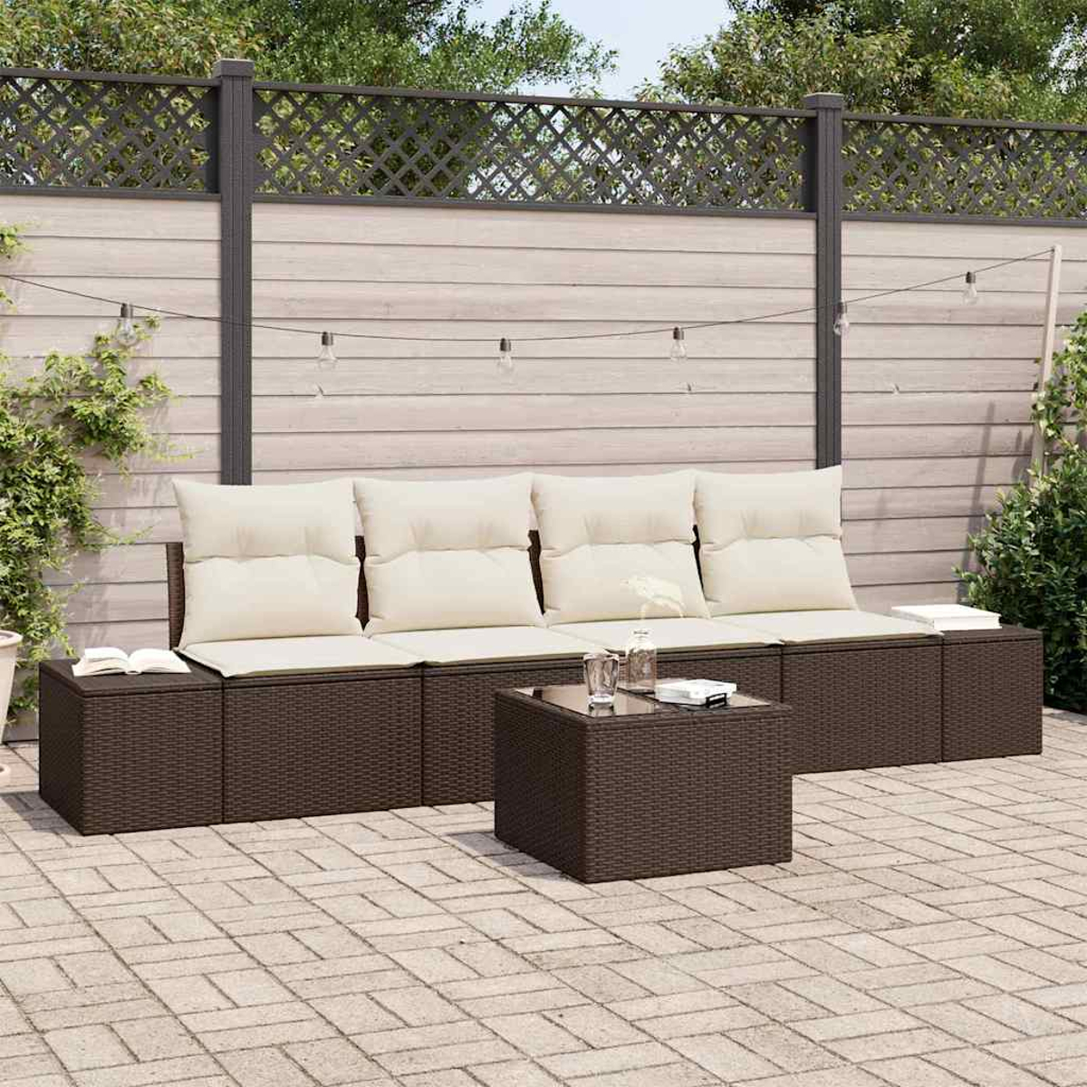 Gartenmöbel: ein braunes Korbmöbel mit cremefarbenen Kissen, Couchtisch, auf einer Backsteinterrasse. Im Hintergrund ein Zaun.