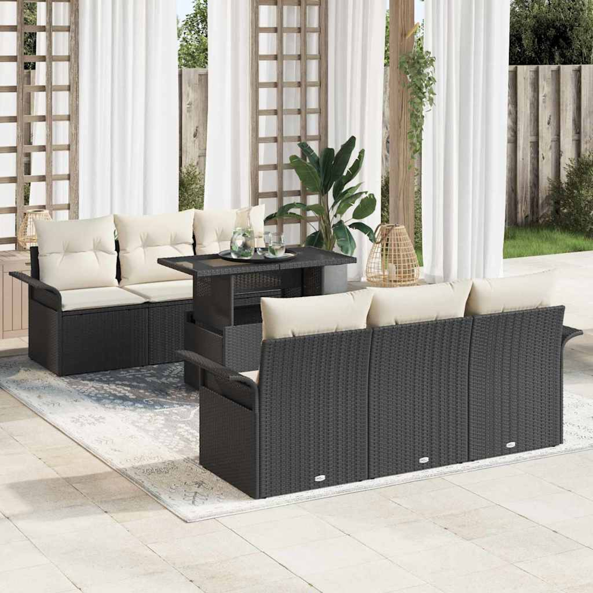 Terrassenset mit schwarzem Korbmöbel, beigen Kissen und einem Tisch mit Glasplatte. Vorhänge und Pflanzen im Hintergrund.