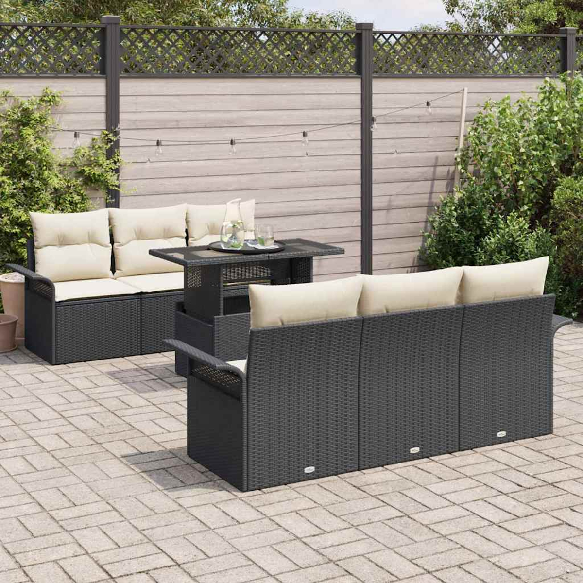 Garten-Set mit schwarzem Korbsessel, Tisch und Stühlen mit cremefarbenen Kissen auf einer Backstein-Terrasse mit Holzzaun.