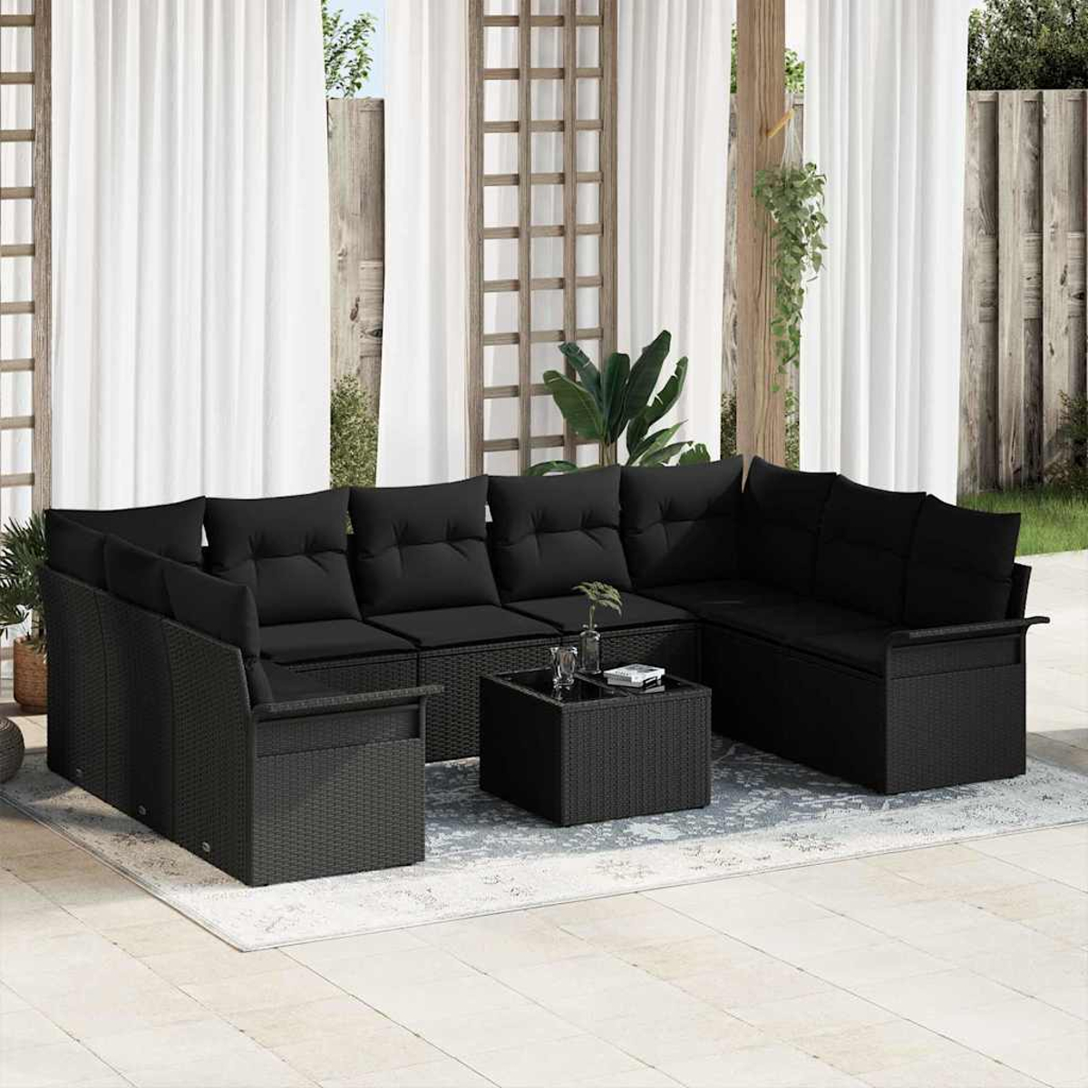 Schwarzes Outdoor-Sofa aus Korbgeflecht mit Kissen, Couchtisch und weißen Vorhängen im Hintergrund. Auf einem Teppich.