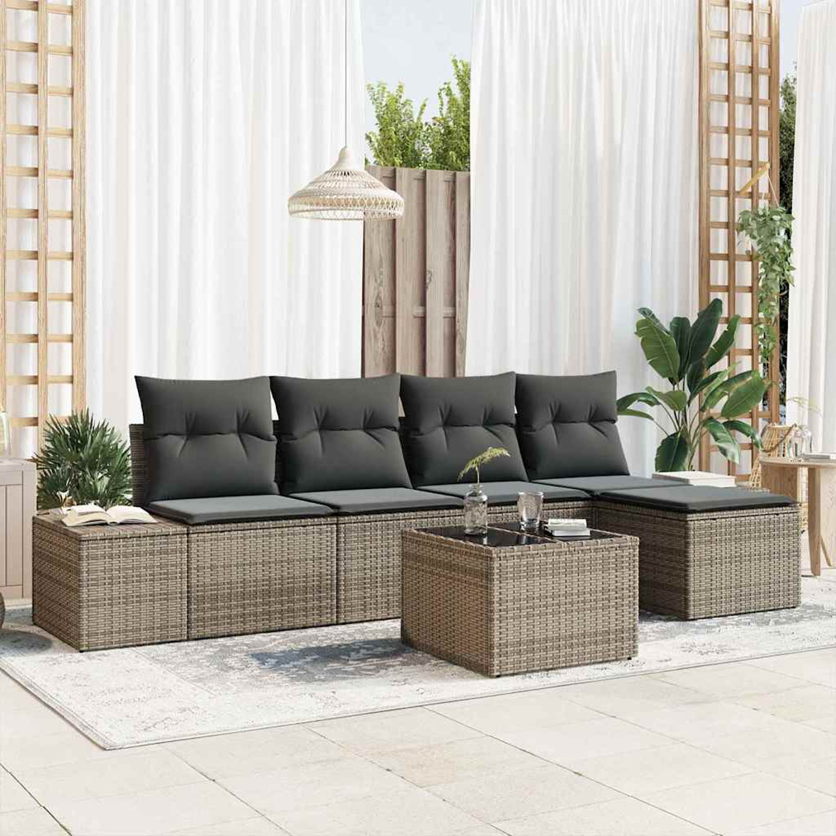 Outdoor-Sitzbereich mit grauen Kissen, einem gewebten Couchtisch und Vorhängen. Pflanzen und eine Hängelampe sind ebenfalls sichtbar.