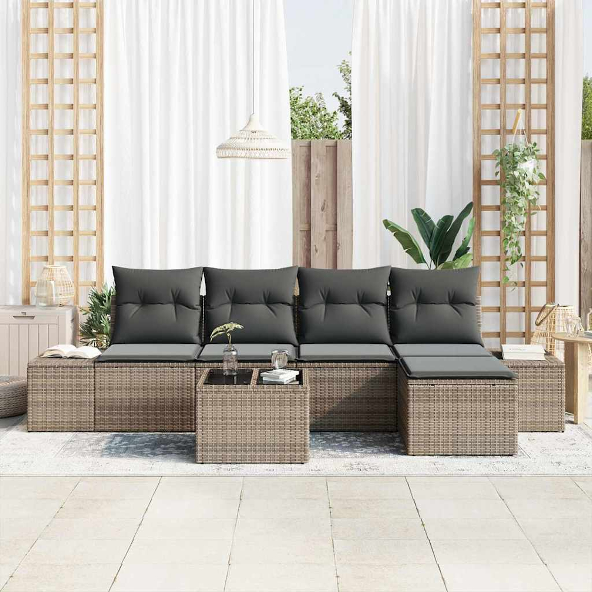Gartenmöbel-Set: graue Kissen, gewebte braune Basis, Glastisch. Weiße Vorhänge, Spalier, Pflanzen und ein weißer Fliesenboden.