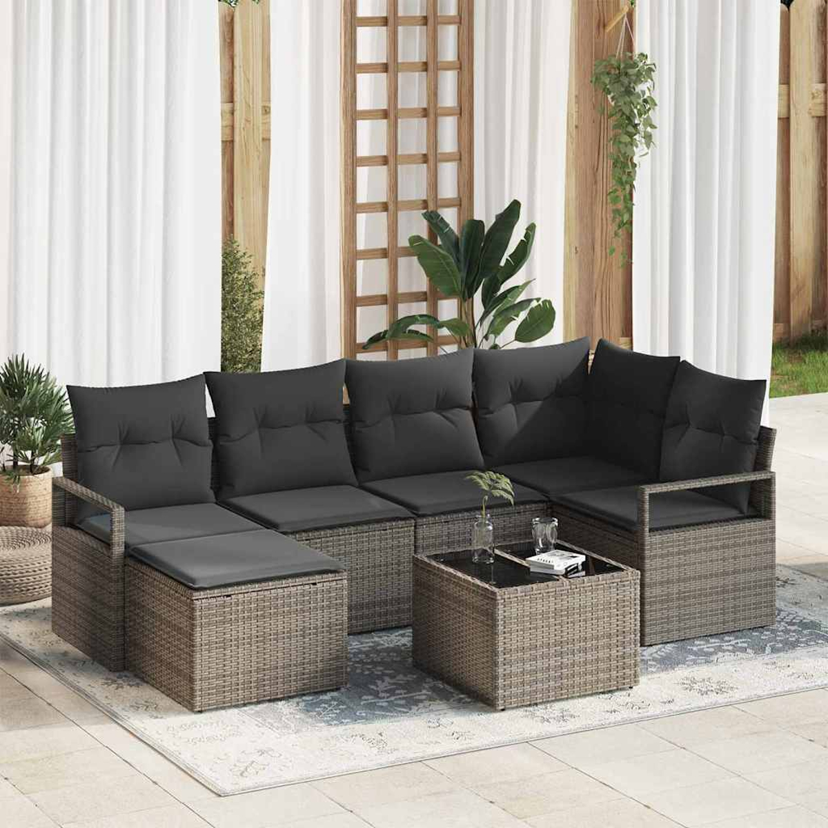 Outdoor-Ecksofa mit grauen Kissen, Couchtisch und Pflanzen. Auf einer Terrasse mit weißen Vorhängen und Holzgitter.