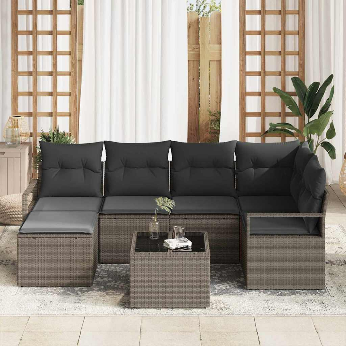 Outdoor-Ecksofa mit dunklen Kissen und einem kleinen Tisch. Das Sofa ist korbähnlich und grau. Eine Pflanze und Vorhänge im Hintergrund.