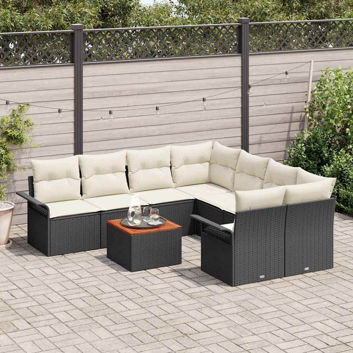 Outdoor-Ecksofa mit Kissen, kleiner Tisch mit Getränken. Terrasse aus Pflastersteinen. Zaun und Grün im Hintergrund.