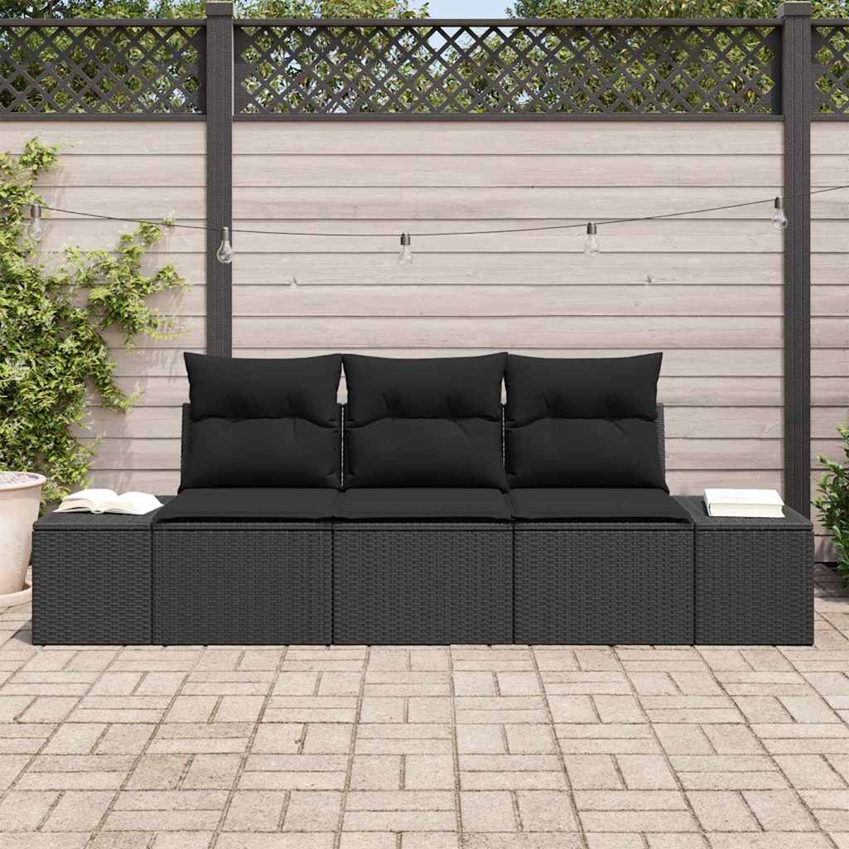 Schwarzes Outdoor-Wicker-Sofa mit schwarzen Kissen. Bücher auf jeder Seite. Holzzaun mit dekorativer Oberseite und Lichterketten im Hintergrund.