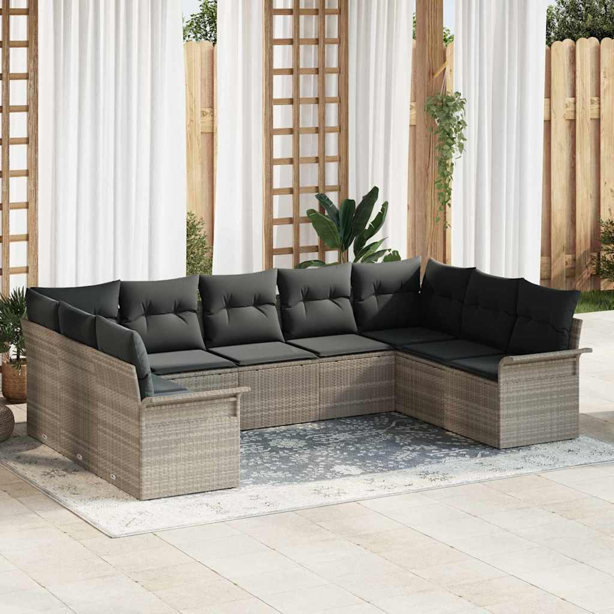 Ein graues Outdoor-Ecksofa aus Korbgeflecht mit schwarzen Kissen steht auf einem Teppich. Weiße Vorhänge und ein Holzzaun sind im Hintergrund.