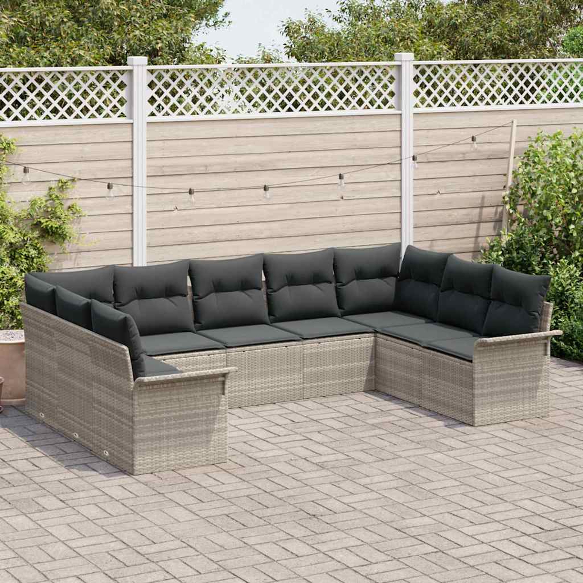 Ein Ecksofa im Freien mit dunkelgrauen Kissen steht auf einer Backstein-Terrasse. Ein weißer Zaun und Grünzeug sind im Hintergrund.