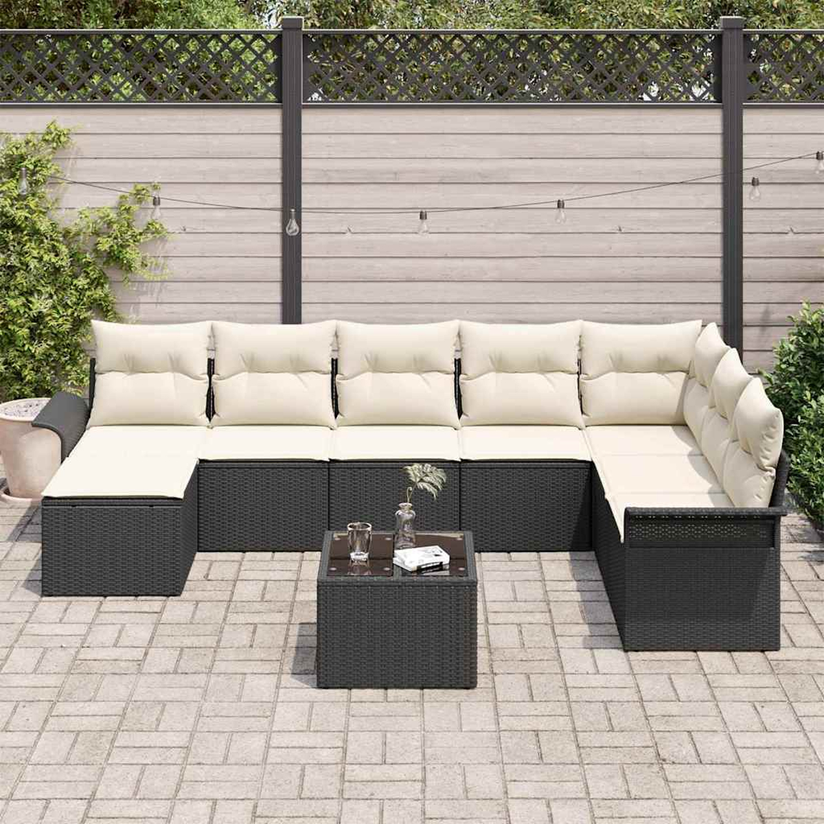 Outdoor-Sitzgruppe mit cremefarbenen Kissen und einem dunkelgrauen Rattanrahmen, Couchtisch und dekorativem Zaun im Hintergrund.