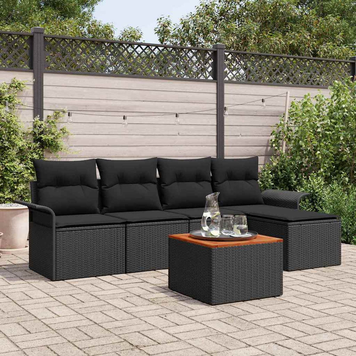 Szene im Freien mit schwarzem Rattansofa, Couchtisch und Holzzaun. Klare Gläser und ein Krug auf dem Tisch.