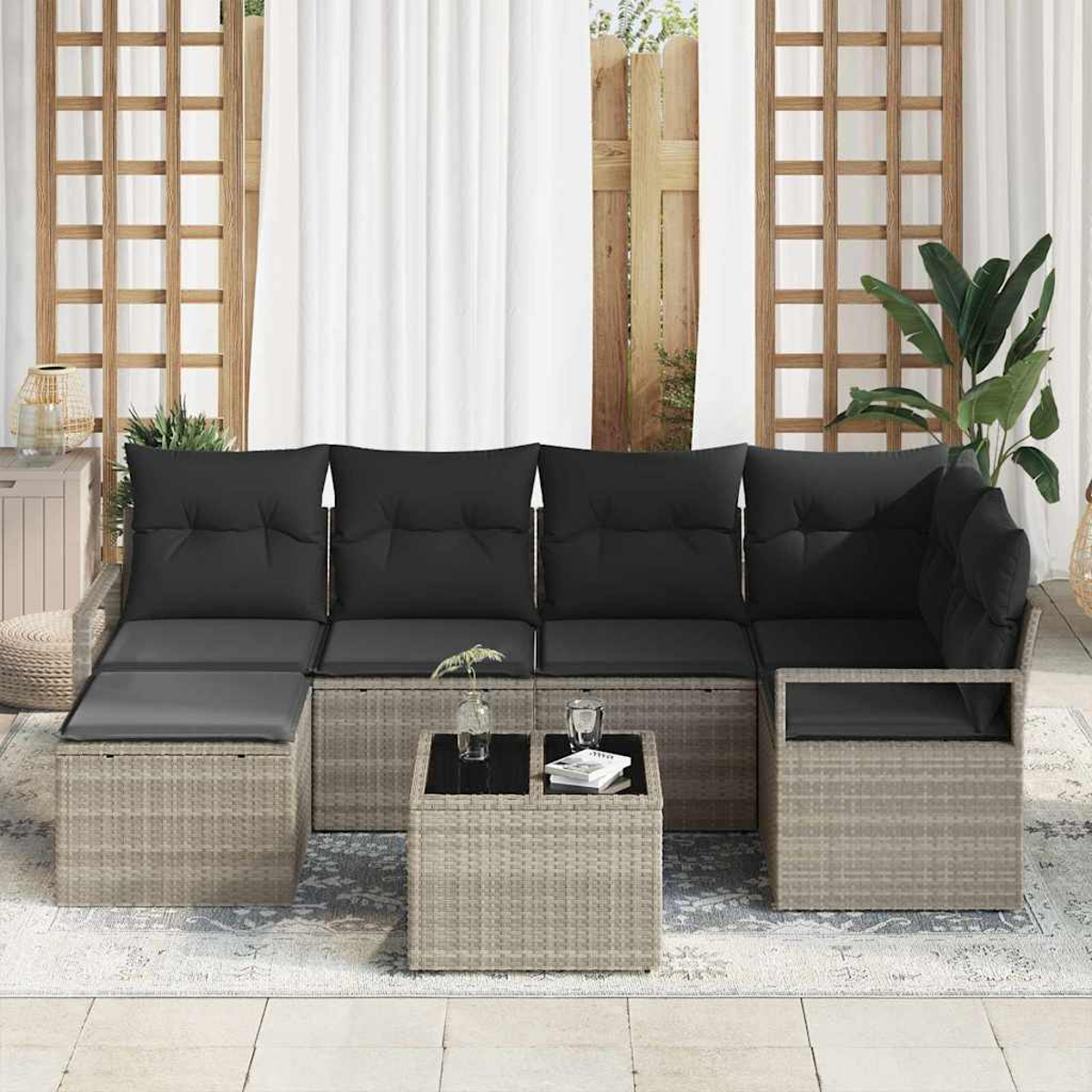 Outdoor-Ecksofa mit schwarzen Kissen und einem kleinen quadratischen Tisch. Die Szene spielt sich auf einem Teppich ab, im Hintergrund weiße Vorhänge.