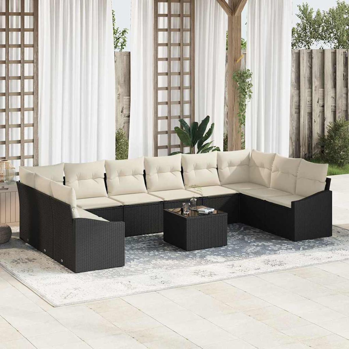 Ein Ecksofa im Freien mit cremefarbenen Kissen und einem schwarzen Rahmen steht auf einem gemusterten Teppich. Weiße Vorhänge und eine Holzkonstruktion sind zu sehen.
