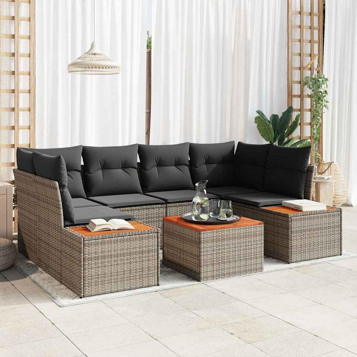 Geflochtenes Ecksofa mit grauen Kissen, zwei Couchtische, Bücher und Gläser. Weiße Vorhänge im Hintergrund. Eine Hängelampe hängt.