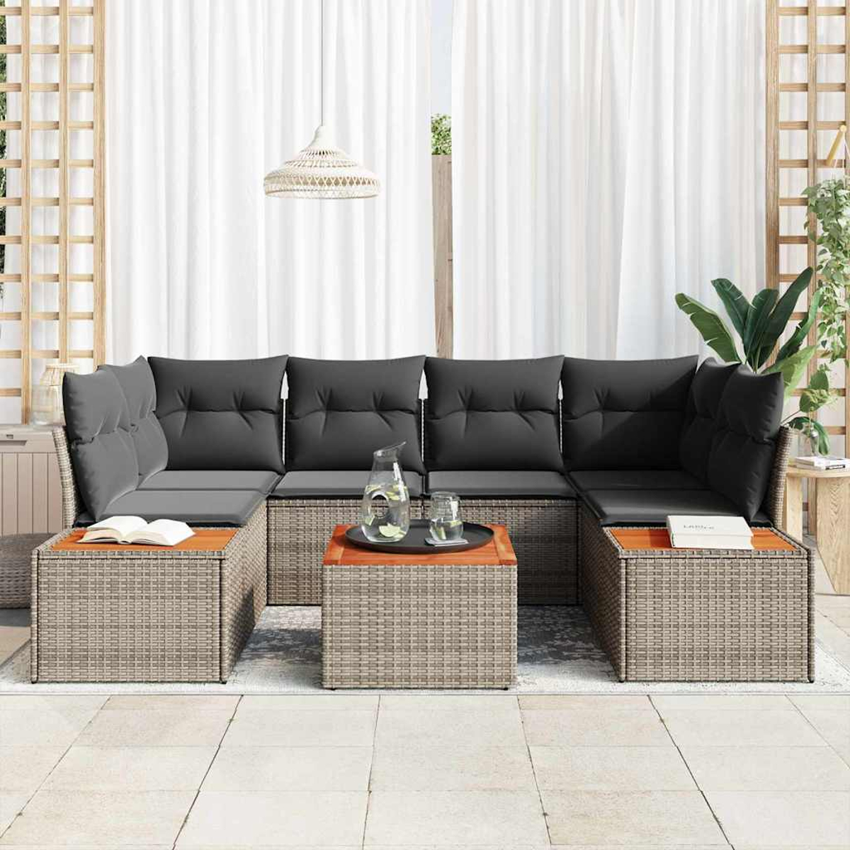 Garten-Sitzgruppe mit grauen Kissen und Holztischen. Weiße Vorhänge im Hintergrund. Glas Wasser und Kanne auf dem Tisch.