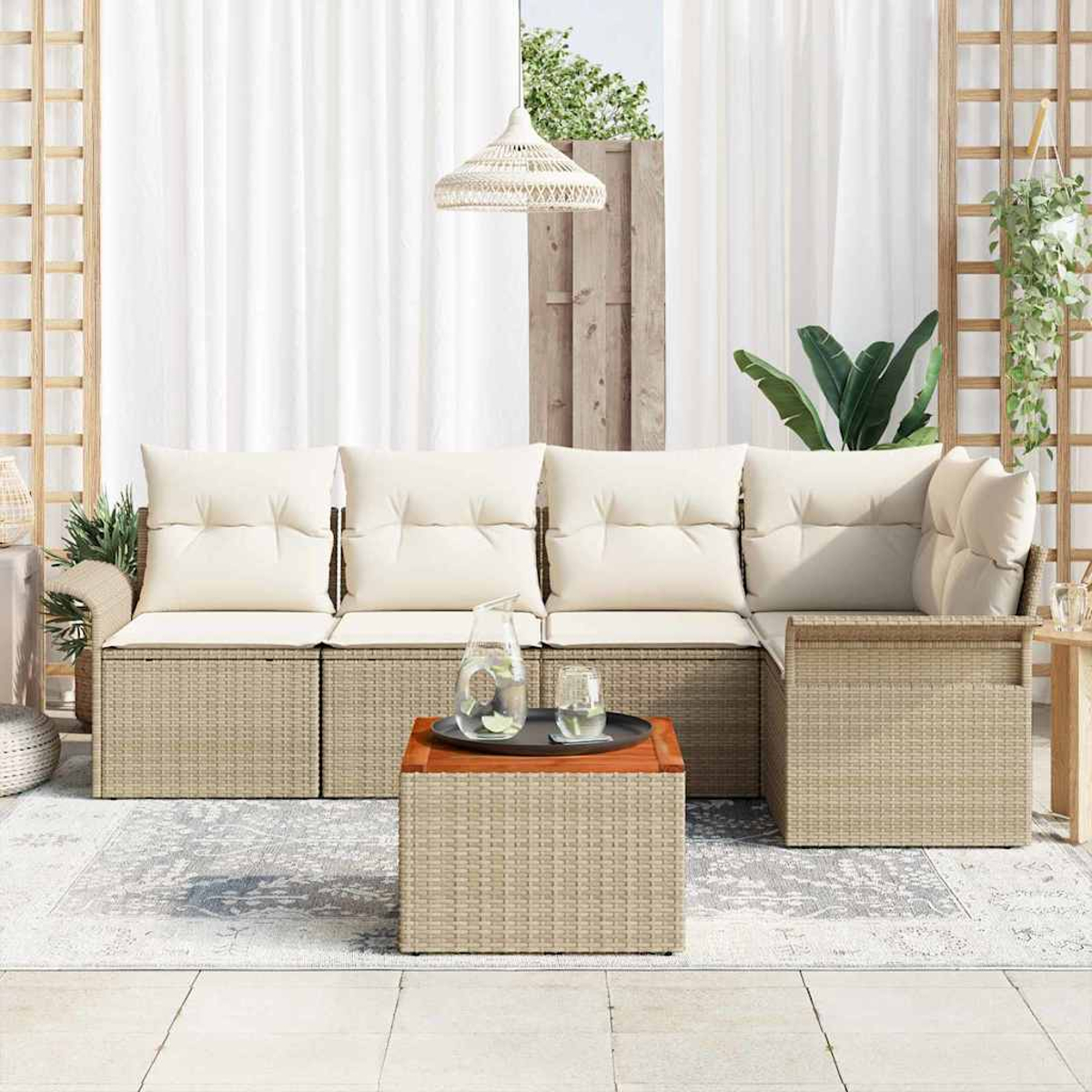 Rattansofa im Freien mit cremefarbenen Kissen. Holztisch mit Glas und Krug. Weiße Vorhänge im Hintergrund.