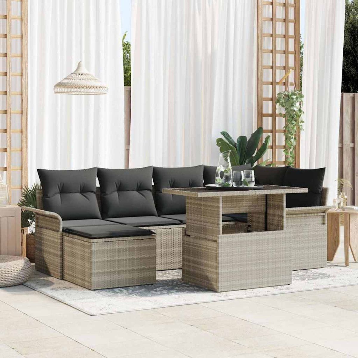Terrassen-Set: graue Kissen auf hellbraunen Korbs Sofas, Tisch mit Hebefunktion, weiße Vorhänge, Hängelampe. Pflanzen und Gläser auf dem Tisch.