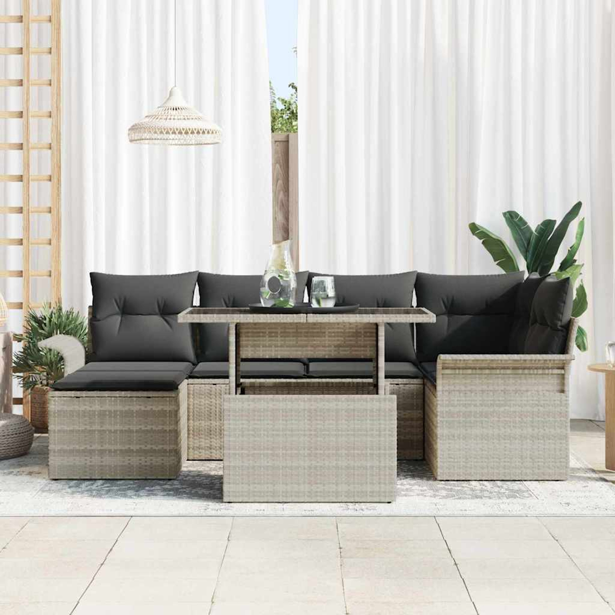 Gartenmöbel-Set aus Weide mit grauen Kissen, Tisch und weißen Vorhängen im Hintergrund. Pflanzen und eine Pendelleuchte sind ebenfalls vorhanden.