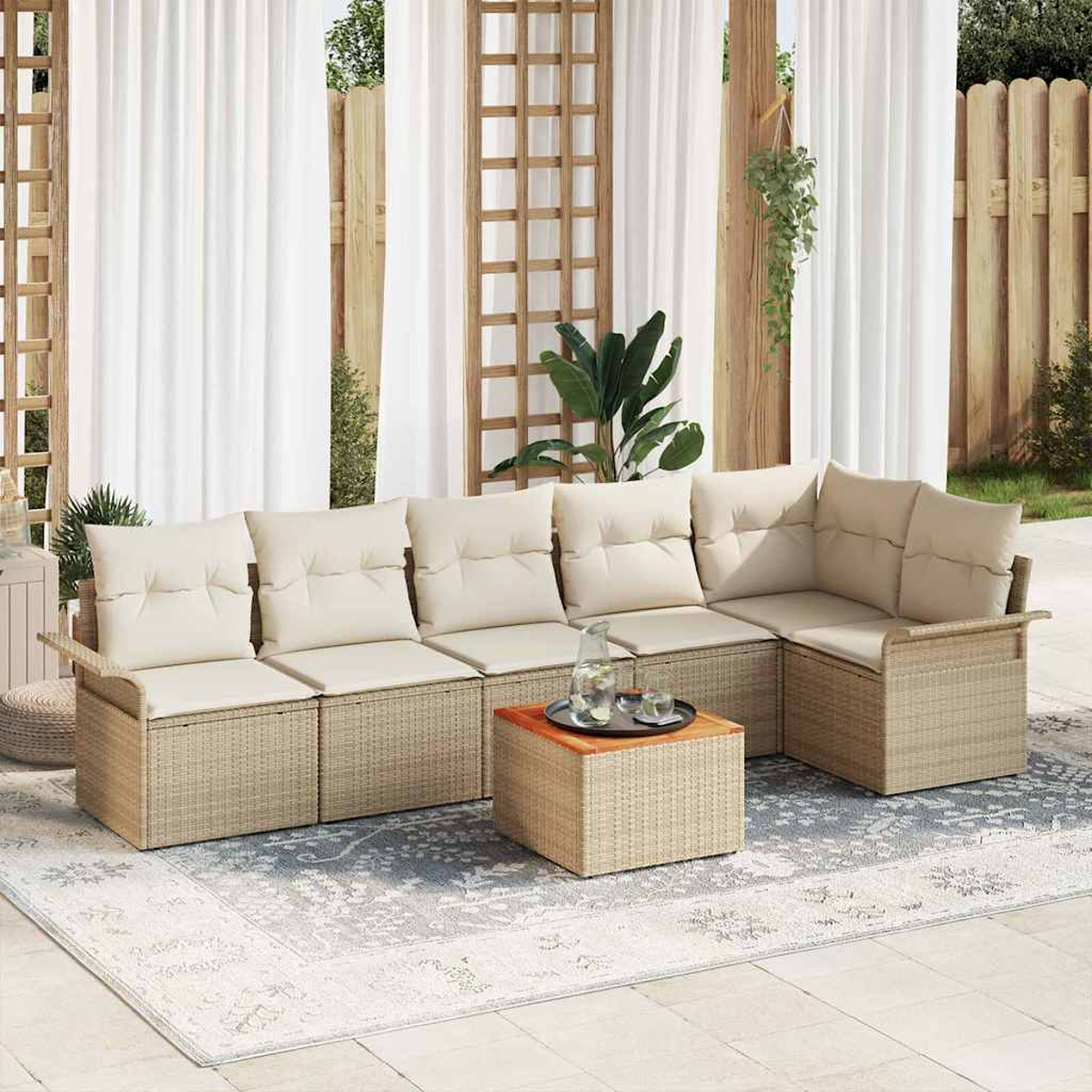 Outdoor-Ecksofa mit cremefarbenen Kissen, Weidenrahmen und Holztisch auf gemustertem Teppich, hinter weißen Vorhängen.