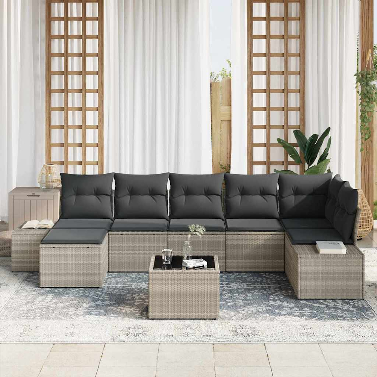 Outdoor-Ecksofa mit grauen Kissen, Couchtisch und Teppich auf einer Terrasse. Weiße Vorhänge und Holzgitter im Hintergrund.