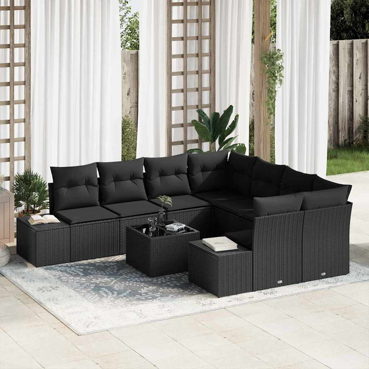 Outdoor-Ecksofa mit schwarzen Kissen. Inklusive Teppich, kleine Tische mit Büchern und Getränken. Weiße Vorhänge und Holzgitter im Hintergrund.