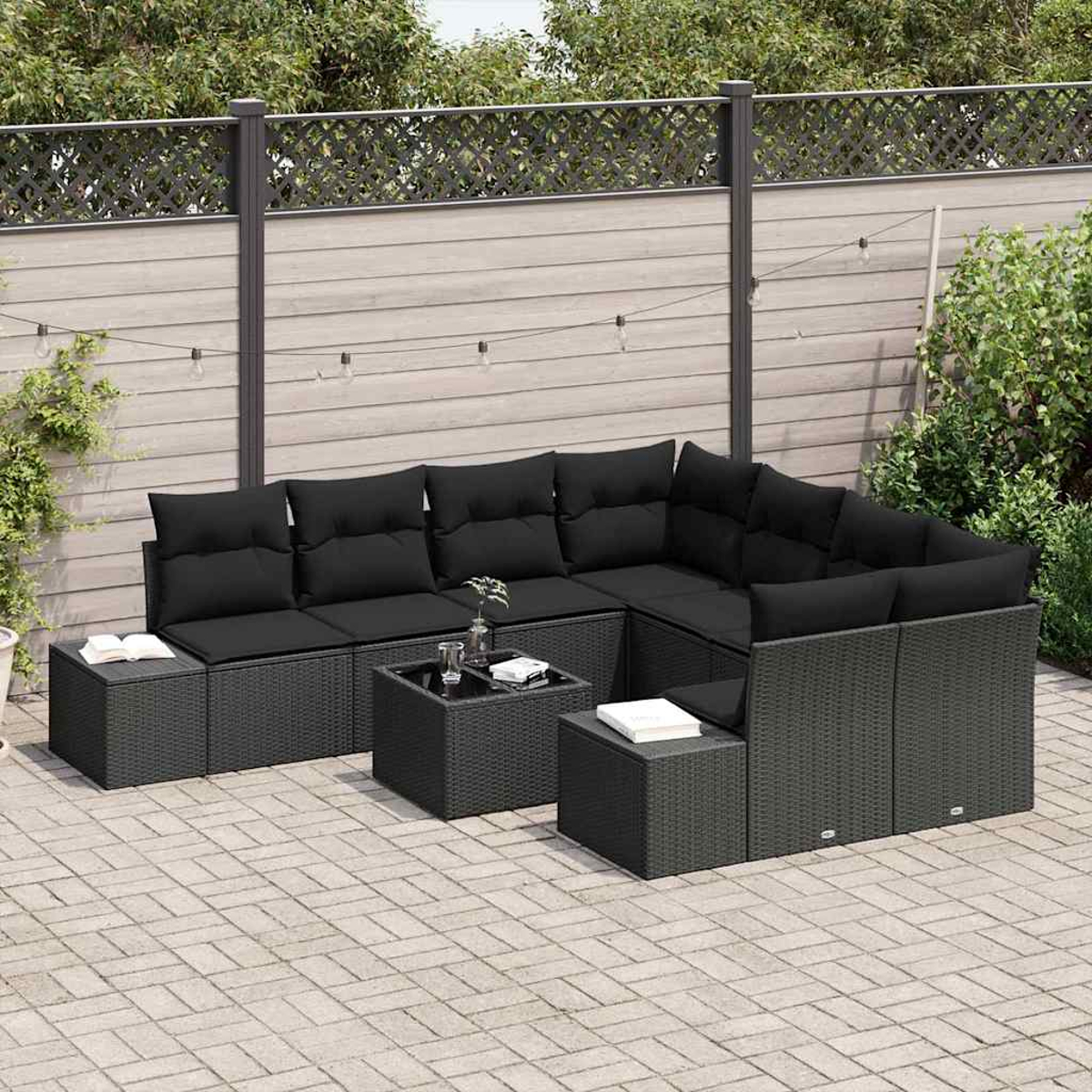 Outdoor-Ecksofa mit schwarzen Kissen und Tischen. Auf einer Ziegelterrasse, mit Holzzaun und Grün im Hintergrund.