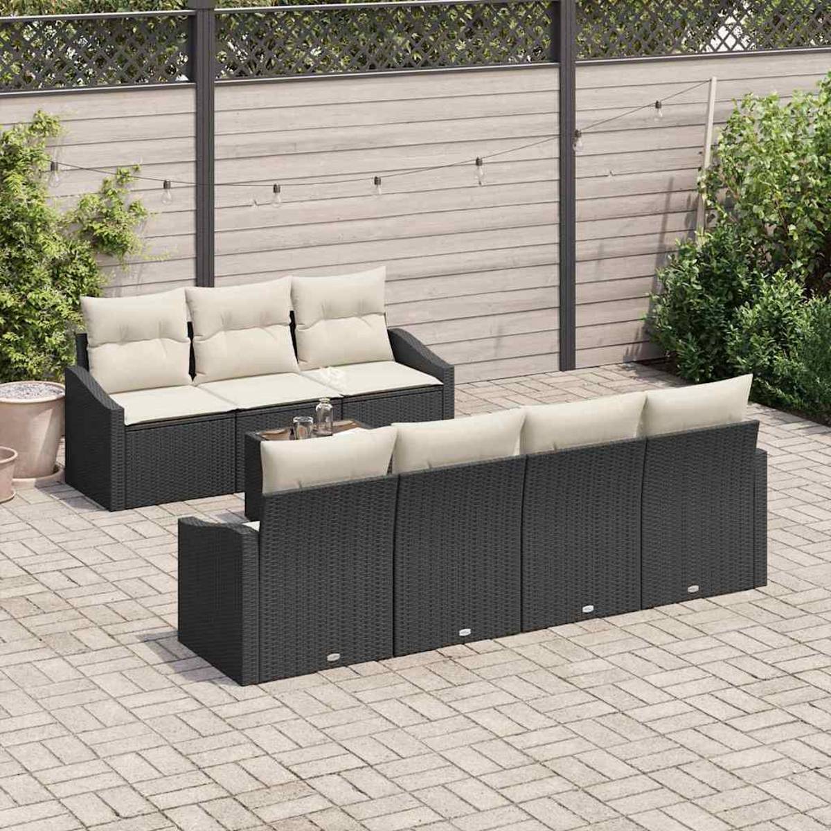 Szene im Freien mit zwei schwarzen Korbs Sofas mit cremefarbenen Kissen. Ein kleiner Tisch mit Getränken steht dazwischen. Im Hintergrund ein Holzzaun.