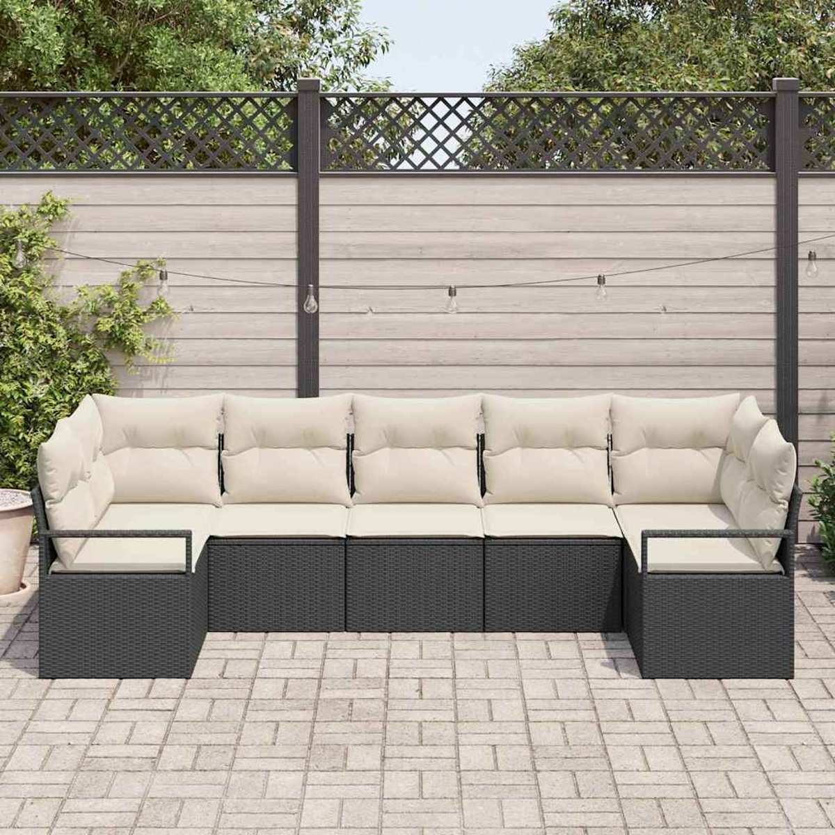 Outdoor-Ecksofa mit cremefarbenen Kissen auf einer Terrasse. Dahinter ein Holzzaun mit Lichterketten und Grün.