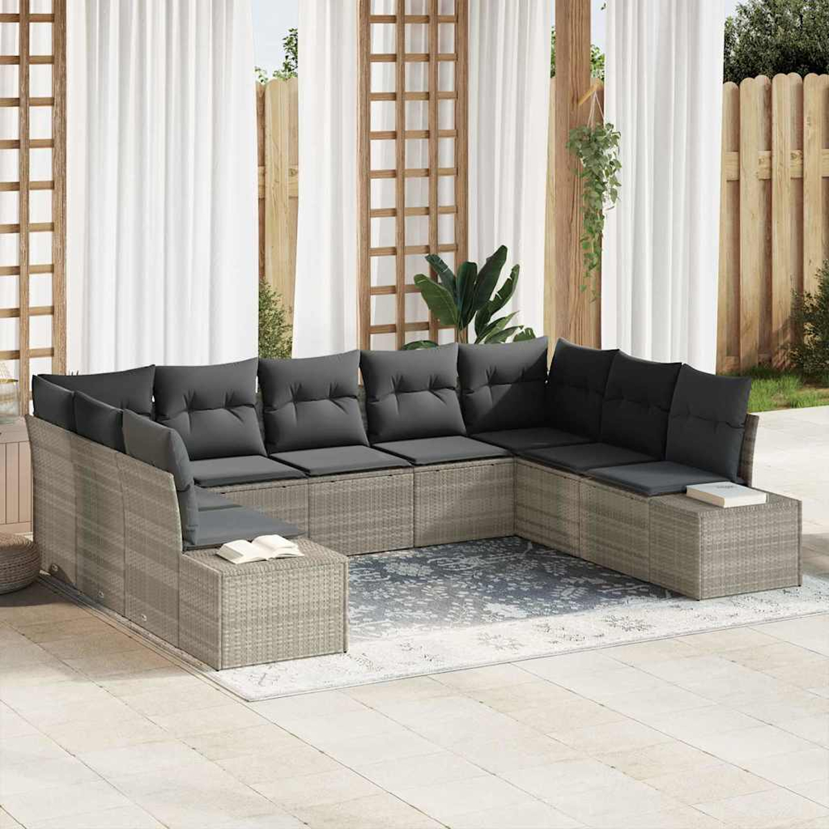 Un sofá seccional de mimbre gris con cojines gris oscuro está en un patio. Cortinas blancas y una valla de madera al fondo.