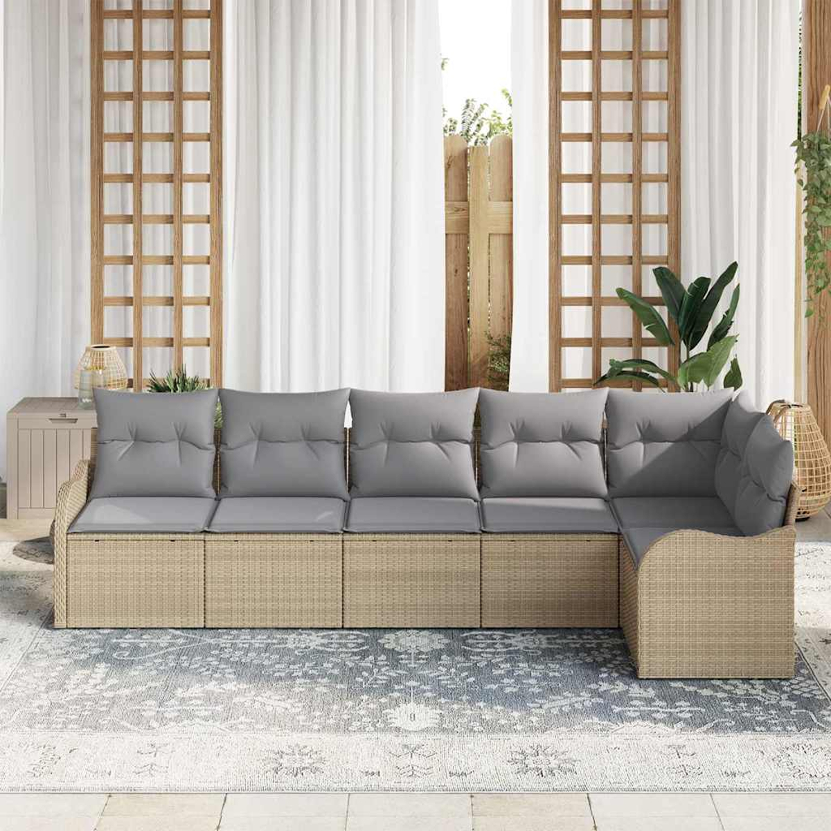 Geflochtenes Sofa mit grauen Kissen auf einem gemusterten Teppich. Holzgitter und weiße Vorhänge im Hintergrund, mit Pflanzen.