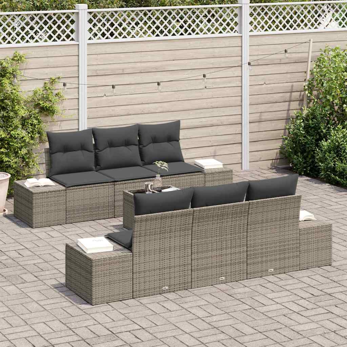 Terrassengarnitur mit grauen Kissen. Das Set umfasst ein Sofa, Stühle und einen Tisch. Im Hintergrund sind ein Zaun und Pflanzen zu sehen.