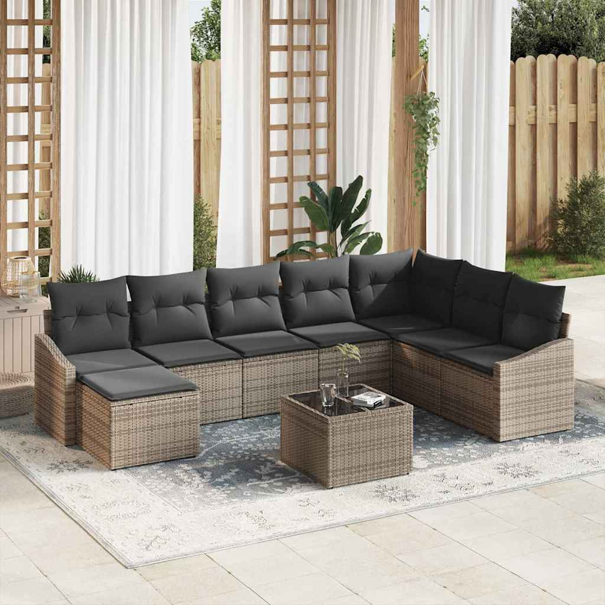 Outdoor-Ecksofa mit grauen Kissen und einem passenden quadratischen Couchtisch auf einem gemusterten Teppich. Weißer Vorhang und Holzzaun im Hintergrund.