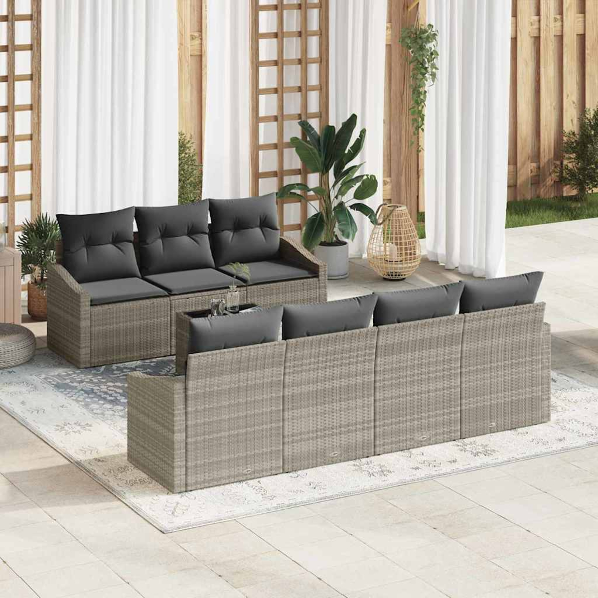 Gartenmöbel-Set. Graue Korbsessel mit dunklen Kissen, Teppich auf gefliestem Patio. Pflanzen und weiße Vorhänge im Hintergrund.