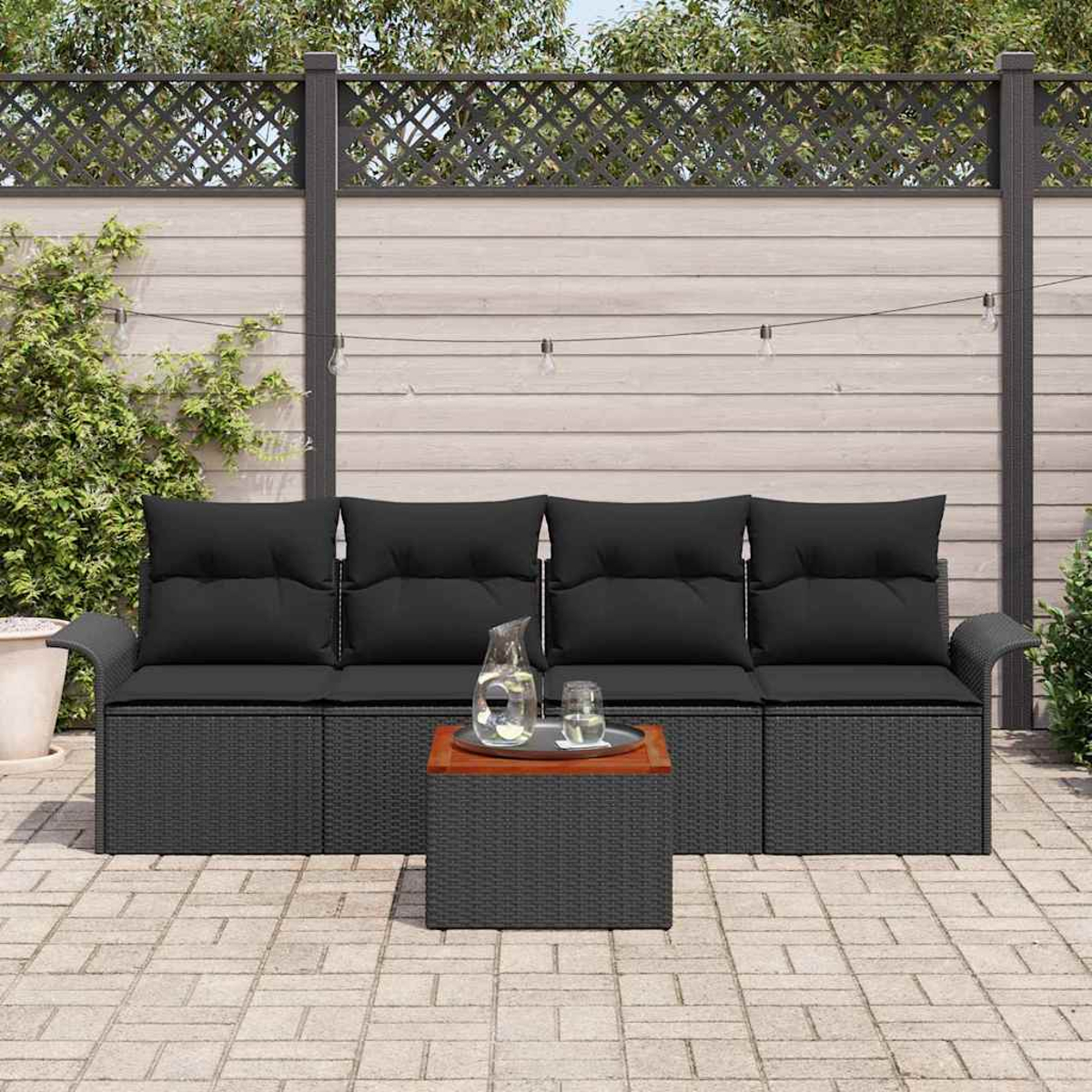 Szene im Freien mit schwarzem Sofa, passendem Couchtisch und Holzzaun. Auf dem Tisch stehen ein Krug und ein Glas.