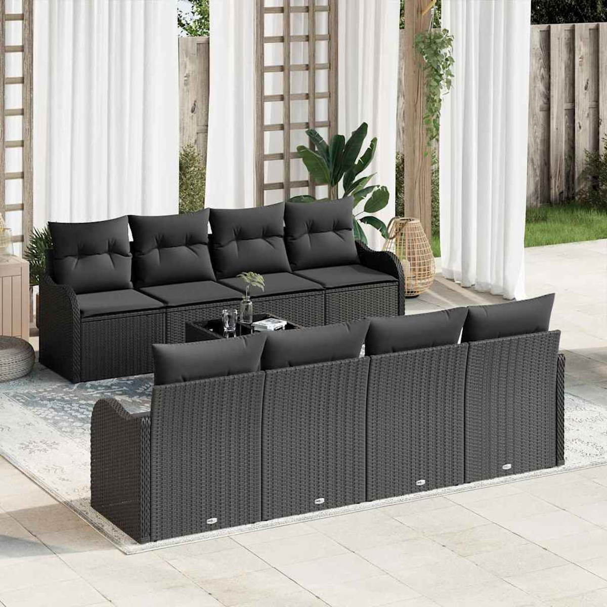 Szene im Freien mit schwarzen Korbsesseln, Kissen und Couchtisch. Weiße Vorhänge und Grün im Hintergrund.