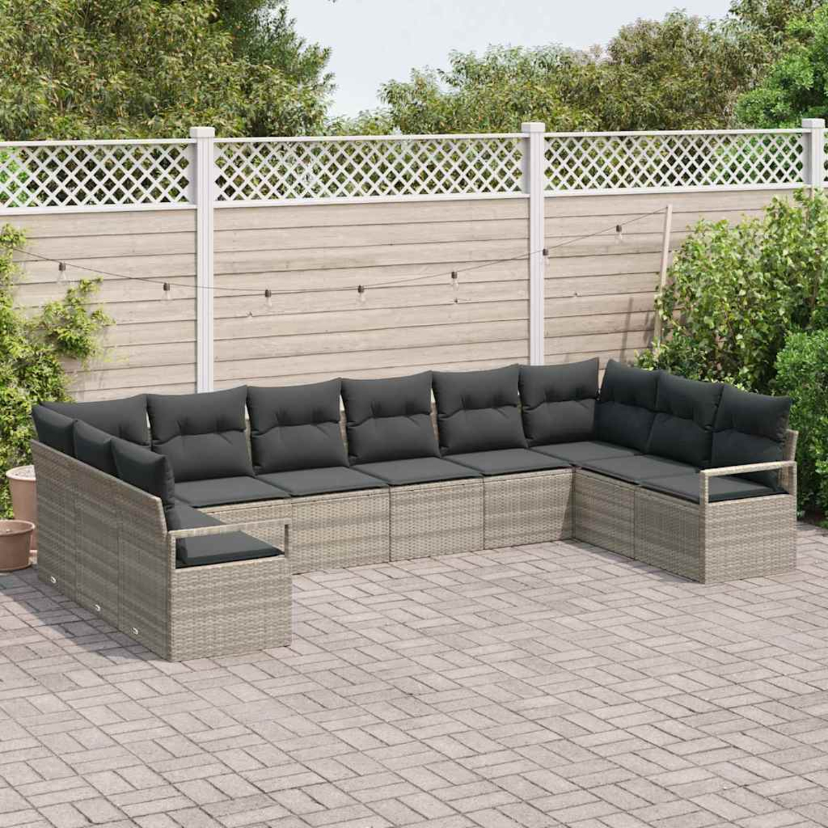 Outdoor-Ecksofa mit grauen Kissen auf einer Terrasse. Ein weißer Gitterzaun und Grünzeug sind im Hintergrund.