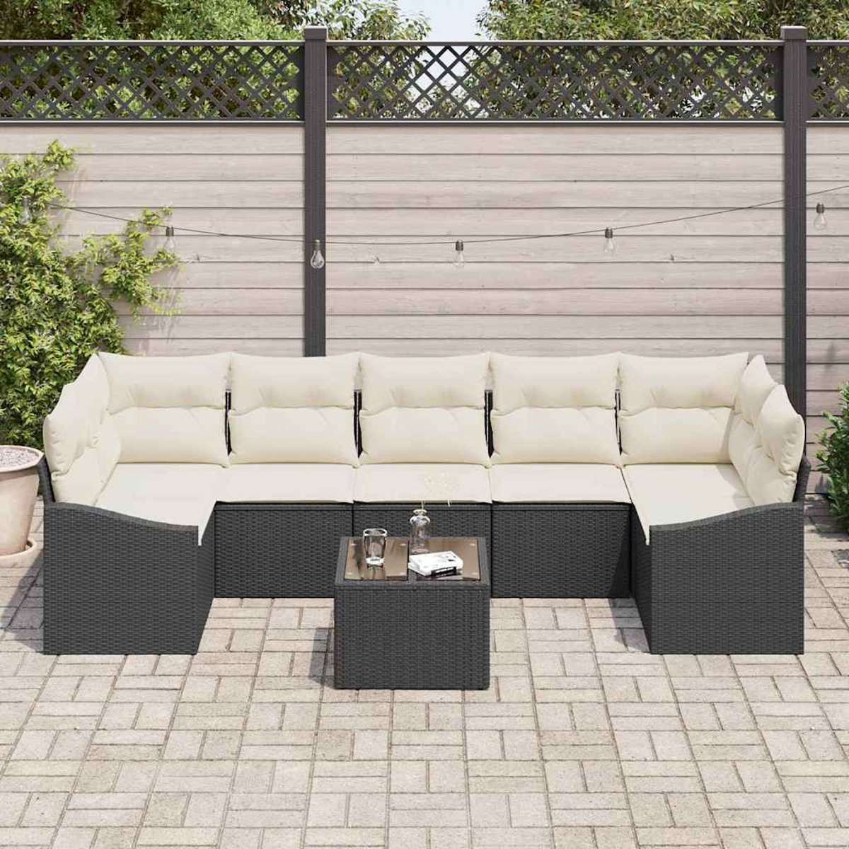 Outdoor-Ecksofa mit cremefarbenen Kissen und einem kleinen Tisch. Der Hintergrund zeigt einen Zaun und Lichterketten.