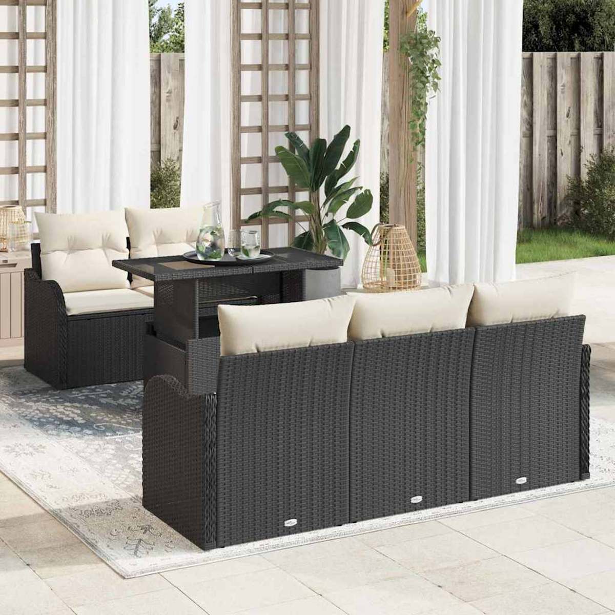 Garten-Terrassenset mit schwarzer Korbmöbel, beigen Kissen und Glastisch. Weiße Vorhänge und Pflanzen im Hintergrund.