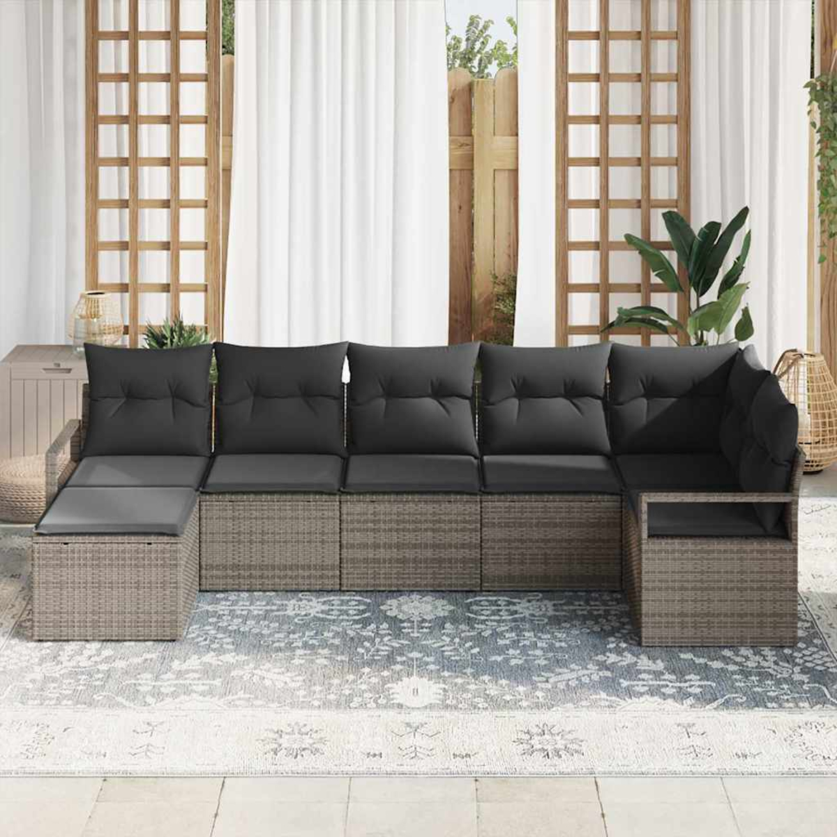 Outdoor-Ecksofa mit grauen Kissen auf einem gemusterten Teppich, vor weißen Vorhängen und einem Holzgitter.