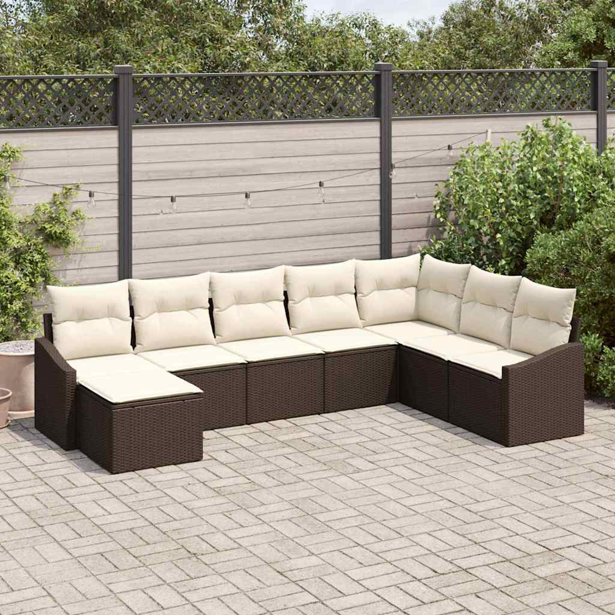 Ein Outdoor-Ecksofa mit cremefarbenen Kissen steht auf einer Ziegelterrasse. Im Hintergrund befinden sich ein Holzzaun und Grün.