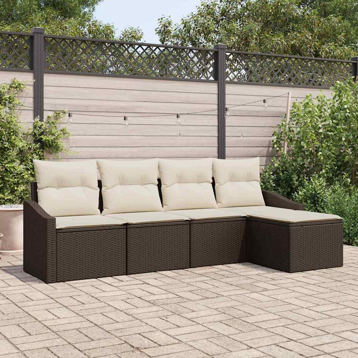 Ein braunes Korbsessel-Sofa mit beigen Kissen steht auf einer Backstein-Terrasse. Im Hintergrund ein Holzzaun mit Grün und Lichtern.