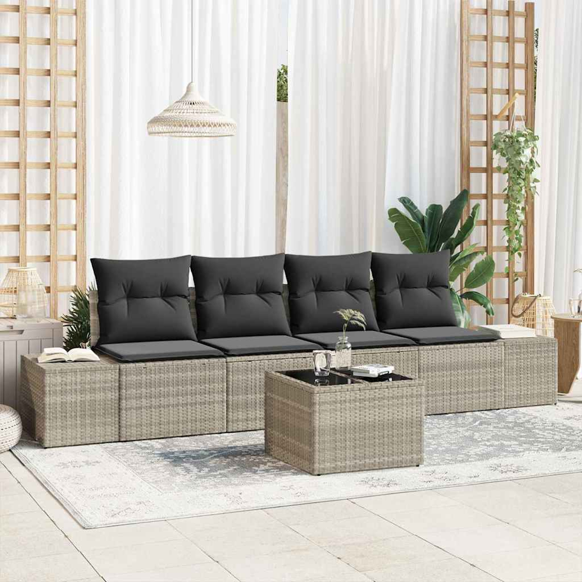 Outdoor-Sitzgruppe mit grauen Kissen, einem kleinen Tisch und einem Teppich. Weiße Vorhänge und Holzgitter im Hintergrund.