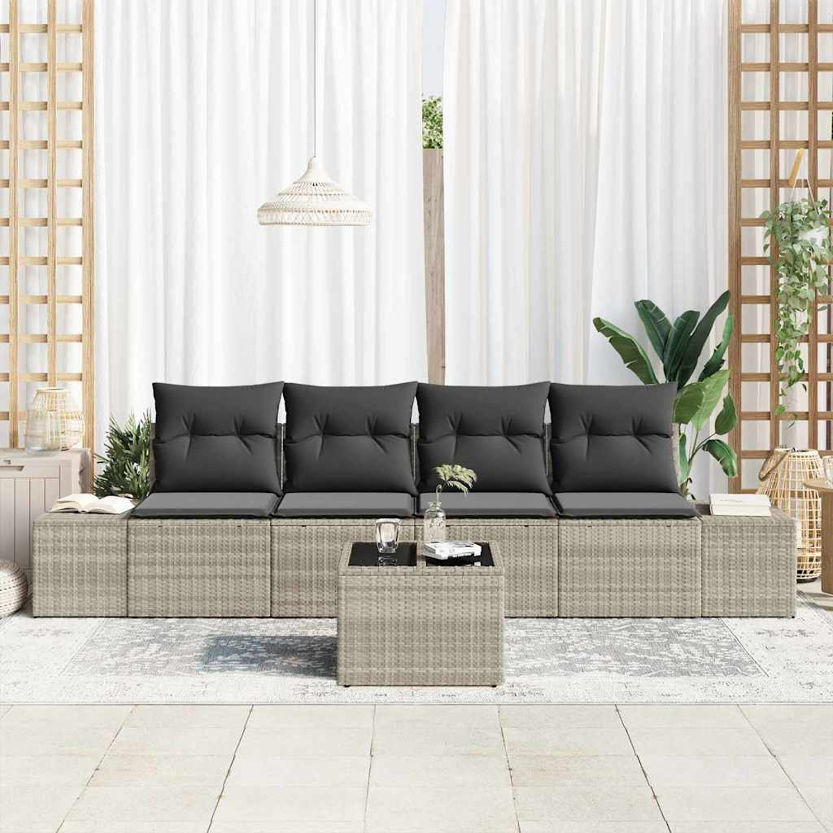 Gartenmöbel mit grauen Kissen, einem kleinen Tisch und weißen Vorhängen. Ein Teppich und Pflanzen sind im Hintergrund.